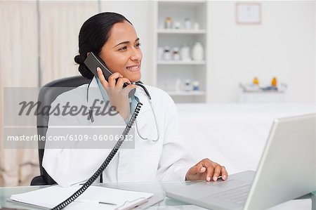 Smiling doctor looking away while sitting in her office and talking on the phone
