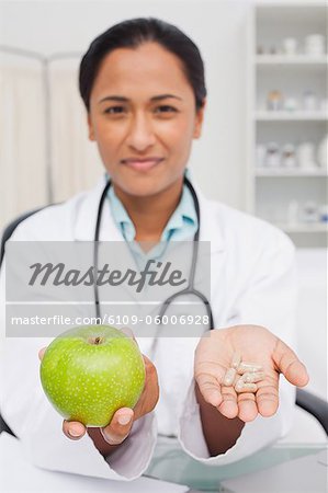 Relaxed nutritionist holding a delicious green apple and vitamins