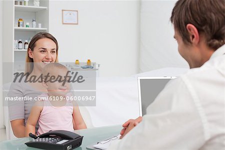Young woman holding her little baby while smiling and looking at the doctor