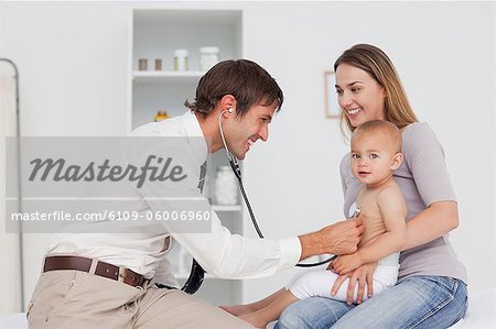 Smiling mother holding her baby being taken her heart beat by the doctor