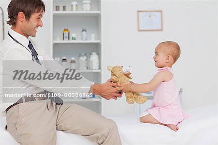 Little baby and her doctor having fun by playing with a teddy bear
