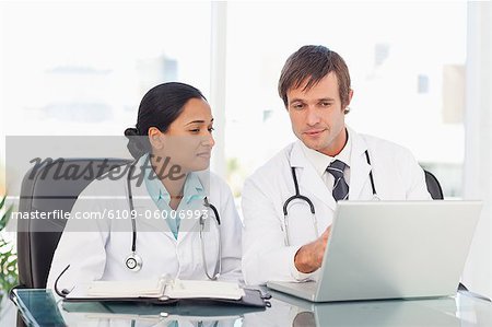Young doctor showing his laptop to his colleague while sitting at a desk