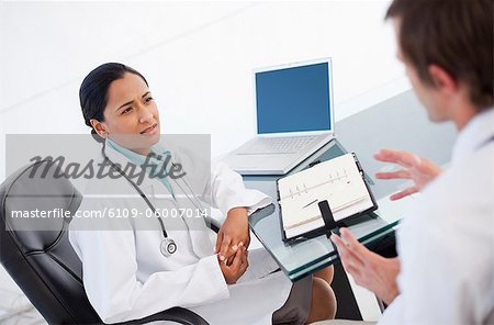 Doctor talking with a colleague while sitting at a desk with a diary