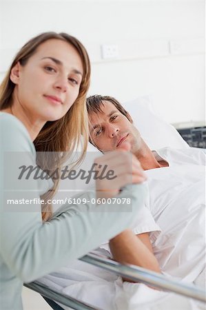 Patient looking at the camera while holding the hand of his wife and lying in a bed