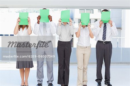 Business team holding green sheets in front of their face as they stand together