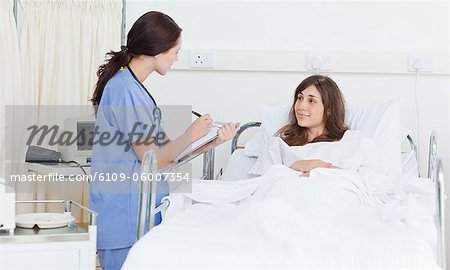 Nurse holding a clipboard as she talks with a patient who is lying in bed
