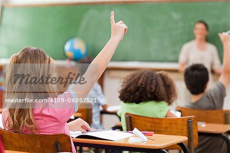Back view of little girl raising hand in class