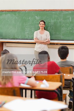 Elementary teacher next to blackboard with arms folded