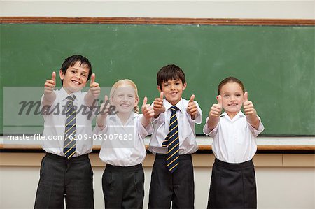 Smiling little children in school uniforms giving thumbs up