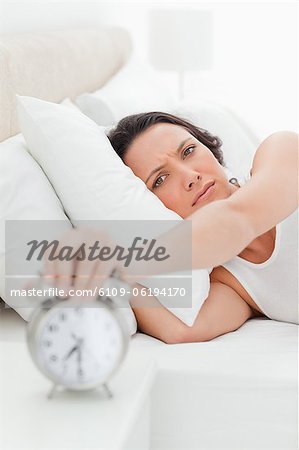 Close-up of a young woman in her bed turning off her alarm clock