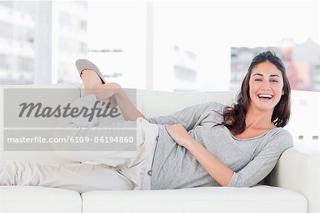 Portrait of a laughing brunette stretching on her sofa