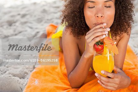 Young relaxed woman sipping a fruit cocktail while lying on the beach