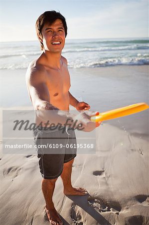 Young attractive man playing frisbee on the beach