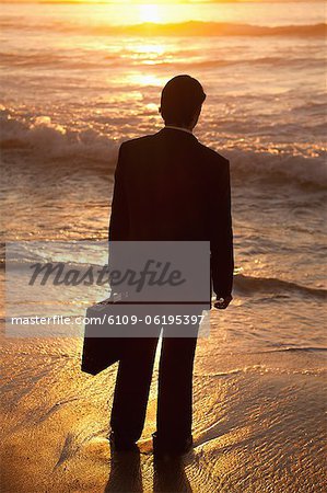 Young businessman standing up on the beach at sunset