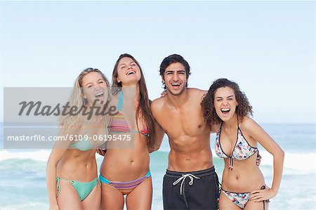 Four friends laughing as they hold each other by the sea