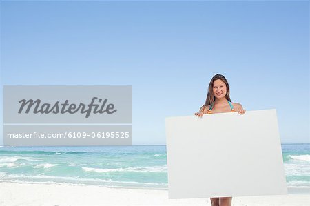 Woman wearing a bikini holding a blank poster in front of her