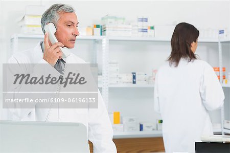 Pharmacist talking on the phone in a pharmacy with an other pharmacist