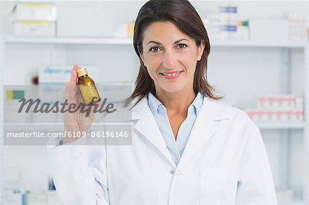 Smiling female pharmacist holding pills and standing in a pharmacy