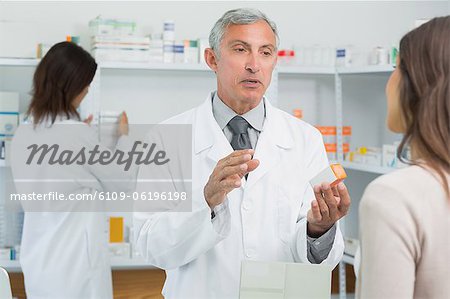 Pharmacist holding a box of pills while talking to a customer