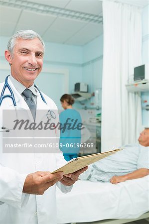 Smiling doctor looking at a chart in a bed ward