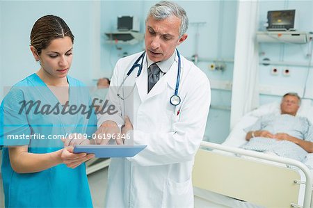 Nurse and doctor touching a tactile tablet in a hospital with two patients