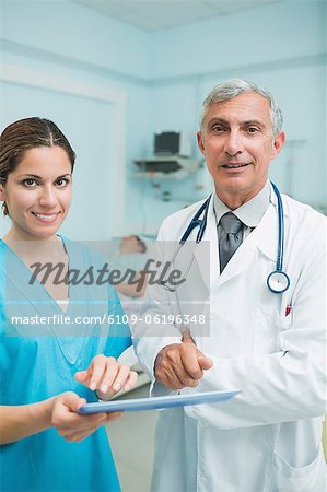 Smiling nurse and a doctor touching a tactile tablet in a hospital with patient