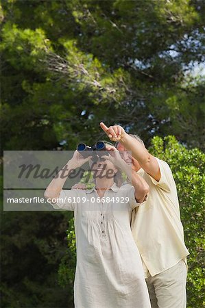 Happy older couple with binoculars with man pointing