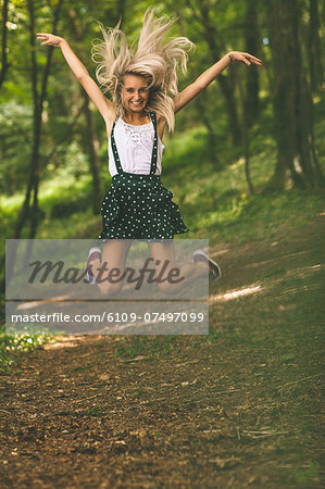 Excited gorgeous blonde jumping in the air in the woods