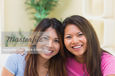 Two young sisters smiling at the camera sitting on a couch in the living room