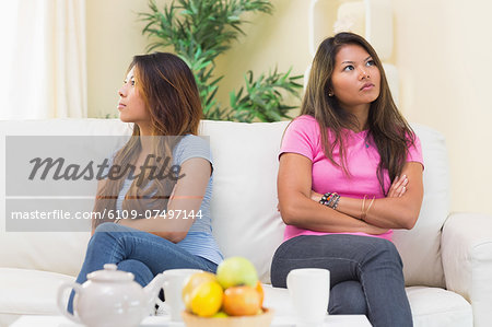 Two displeased sisters sitting on a white couch in the living room Two displeased sisters sitting on a white couch in the living room