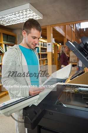 Happy good looking student standing next to photocopier in library in a college