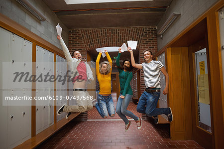 Excited casual students jumping in the air in hallway in a college