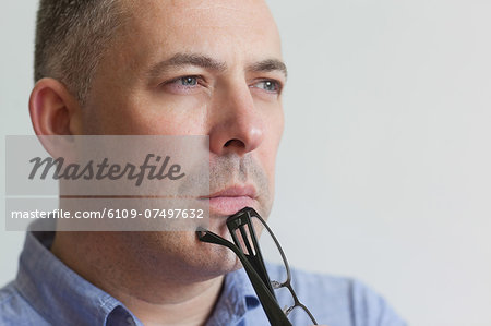 Thinking lecturer standing in his classroom holding his glasses in college