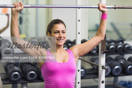 Sporty cheerful brunette holding barbell in weights room of gym