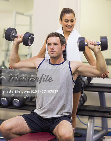 Trainer correcting attractive man lifting dumbbells in weights room of gym