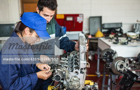 Focused trainee and instructor checking engine in workshop