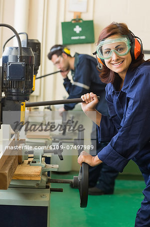 Cheerful trainee with safety glasses drilling wood in workshop