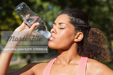 Close up of a tired healthy young woman drinking water in the park