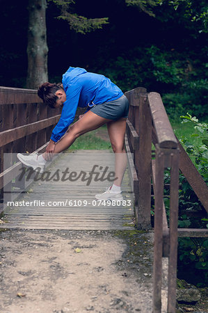 Full length side view of a healthy young woman stretching her leg during exercise on footbridge