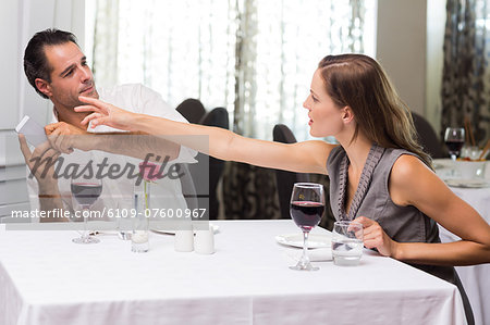 Couple with wine glass and cellphone arguing in restaurant