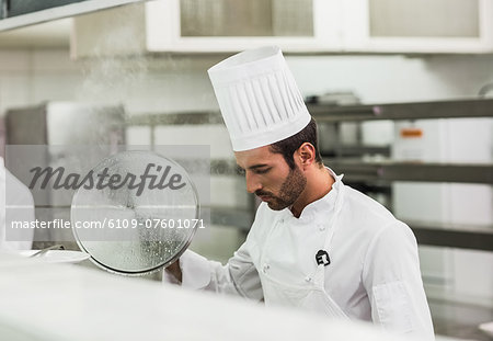 Handsome chef lifting a lid off a pot