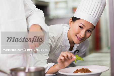 Happy chef putting basil leaf on spaghetti dish