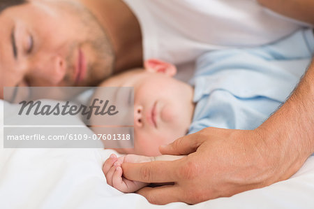 Happy father lying with baby son sleeping