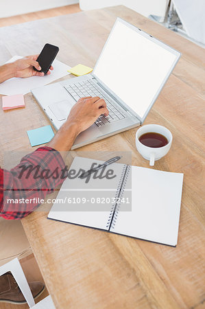 Man typing on laptop and using smartphone at desk Man typing on laptop and using smartphone at desk