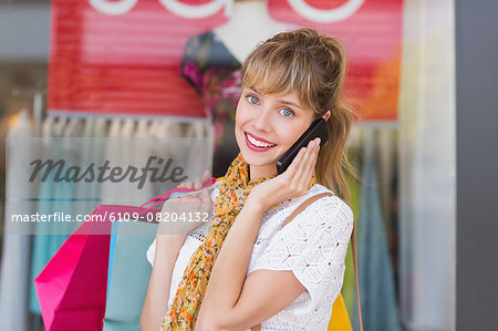 Smiling woman holding shopping bags having a phone call