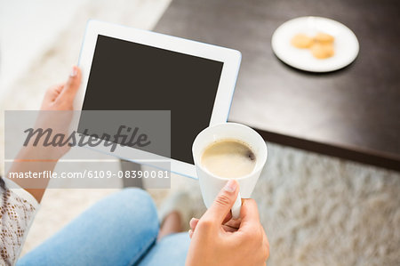 Smiling casual woman using her tablet while holding coffee