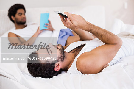 Gay couple reading book and using smartphone