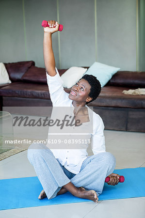 Woman exercising with dumbbells while sitting on mat