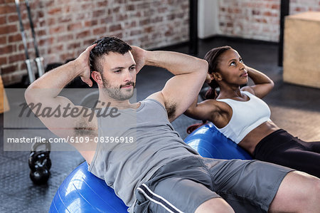 Fit man and woman doing sit ups on exercise ball - Stock Photo