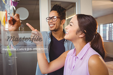 Businessman writing while colleague pointing at sticky notes